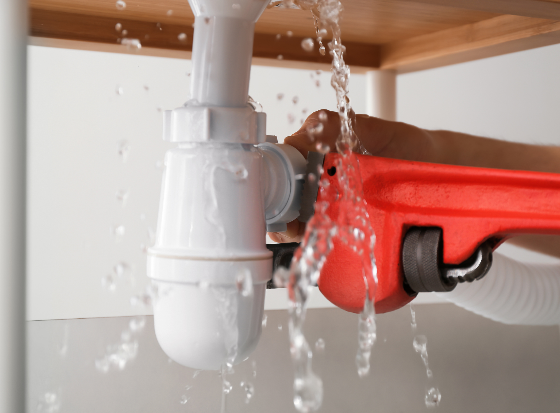 A person is fixing a leaking sink pipe with a wrench.