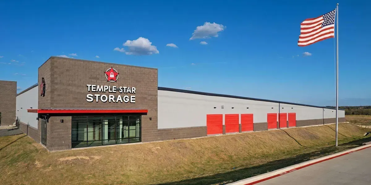 Temple Star Storage building with a brick and gray exterior, red doors, and an American flag, under a blue sky.