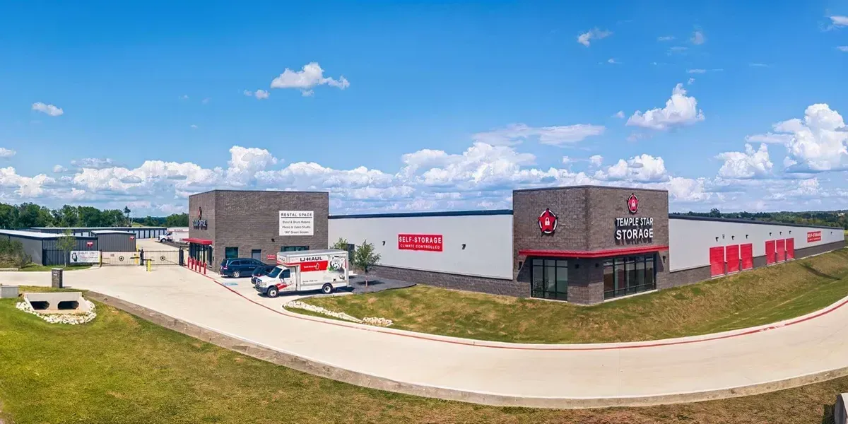 Wide-angle exterior view of a modern brick and white industrial complex with loading bays under a blue sky with clouds.