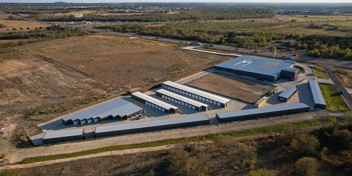 Aerial view of a self-storage facility with multiple rows of storage units and a large warehouse building on a lot.