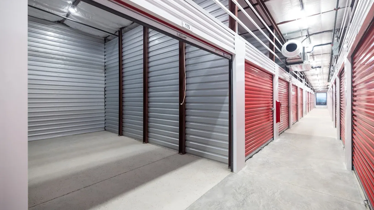 An indoor self-storage facility corridor with grey and red rolling metal doors lining a concrete walkway.