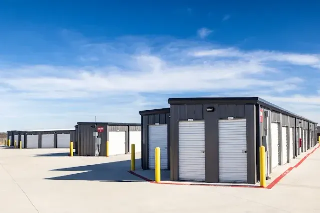 An empty, clean storage unit with light grey metal walls and floor, flanked by closed red roll-up doors.