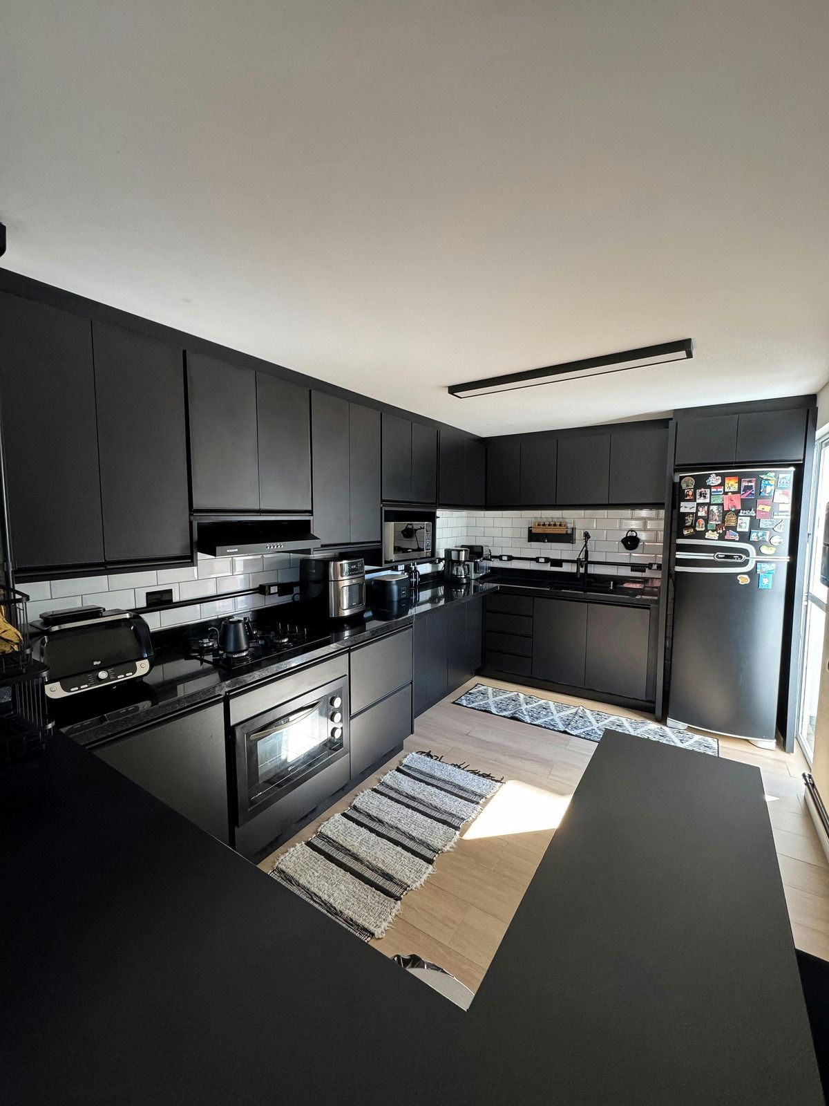 Black modern kitchen with matching cabinetry, appliances, and countertops; small rug and window.