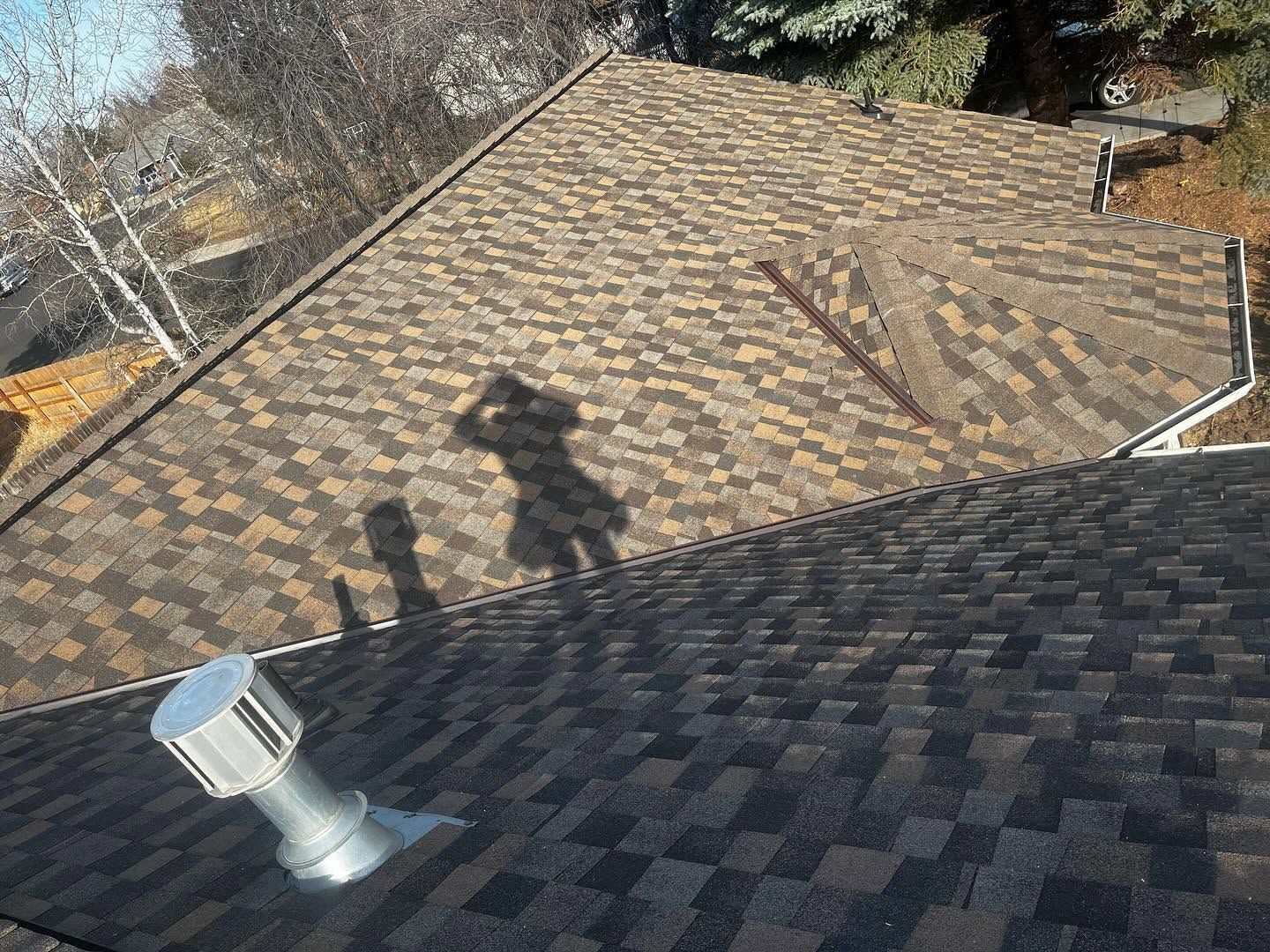 Rooftop with tan and dark shingles, a silver vent, and shadows cast across the roofline.