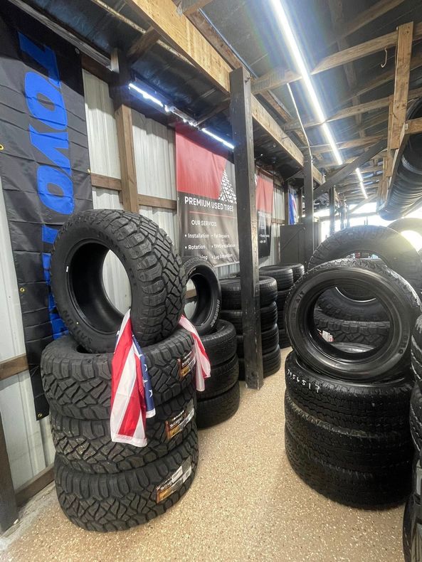 Tire shop interior with neatly stacked tires and technician assisting a customer