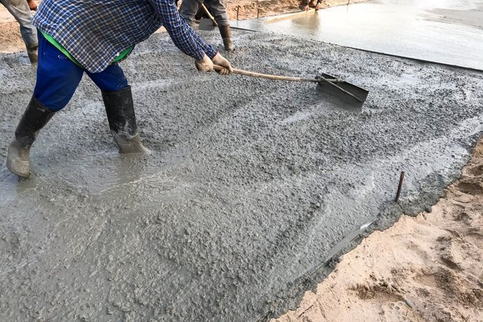 Construction worker using a rake to level wet concrete on a construction site. They are wearing work clothes.