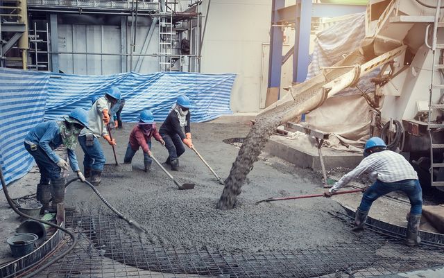 Construction workers smoothing wet concrete from a truck. They wear hard hats, and the scene is outdoors on a construction site.