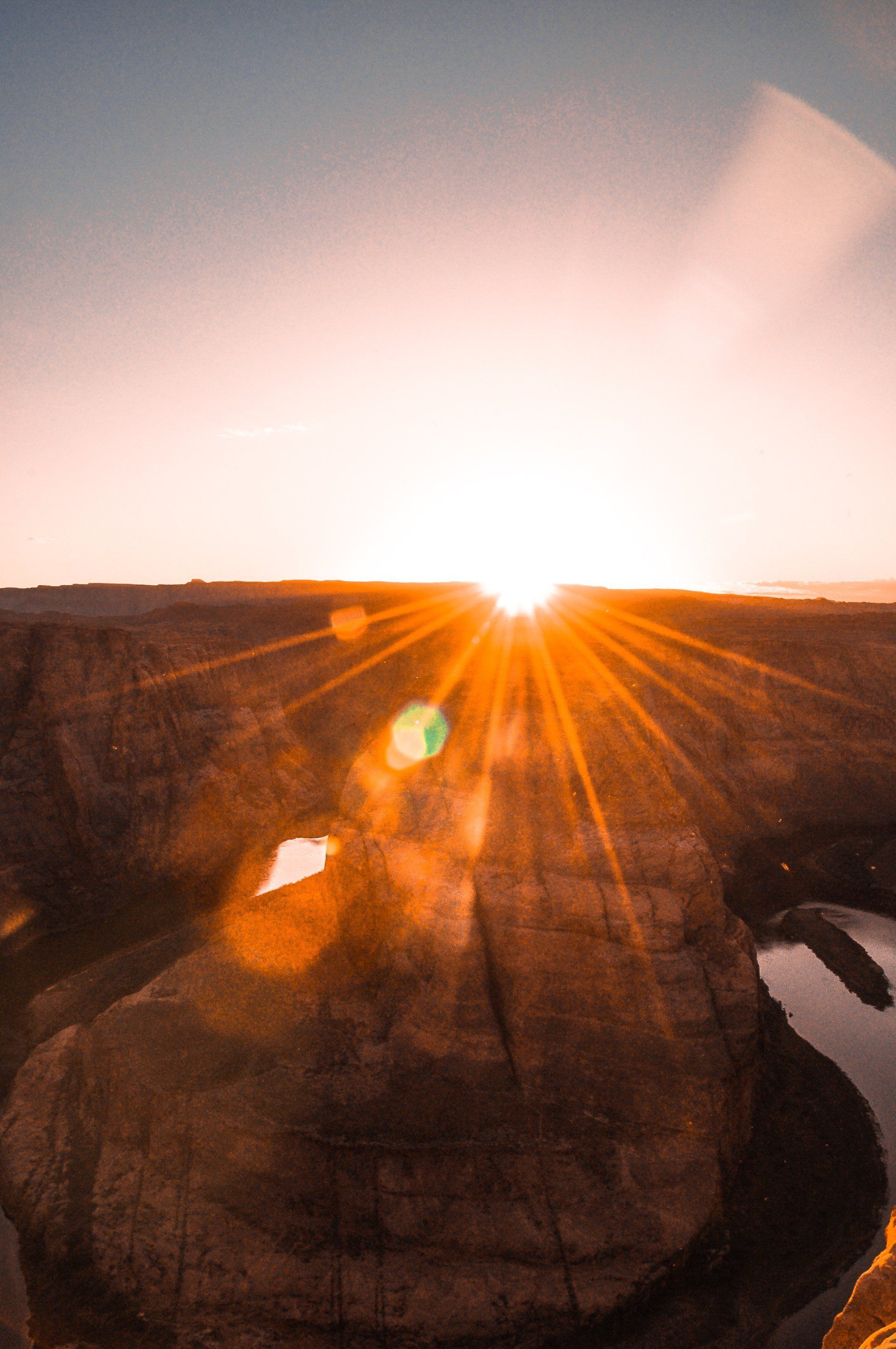 Sunrise over a rocky canyon, with bright orange sun rays and a winding river below.