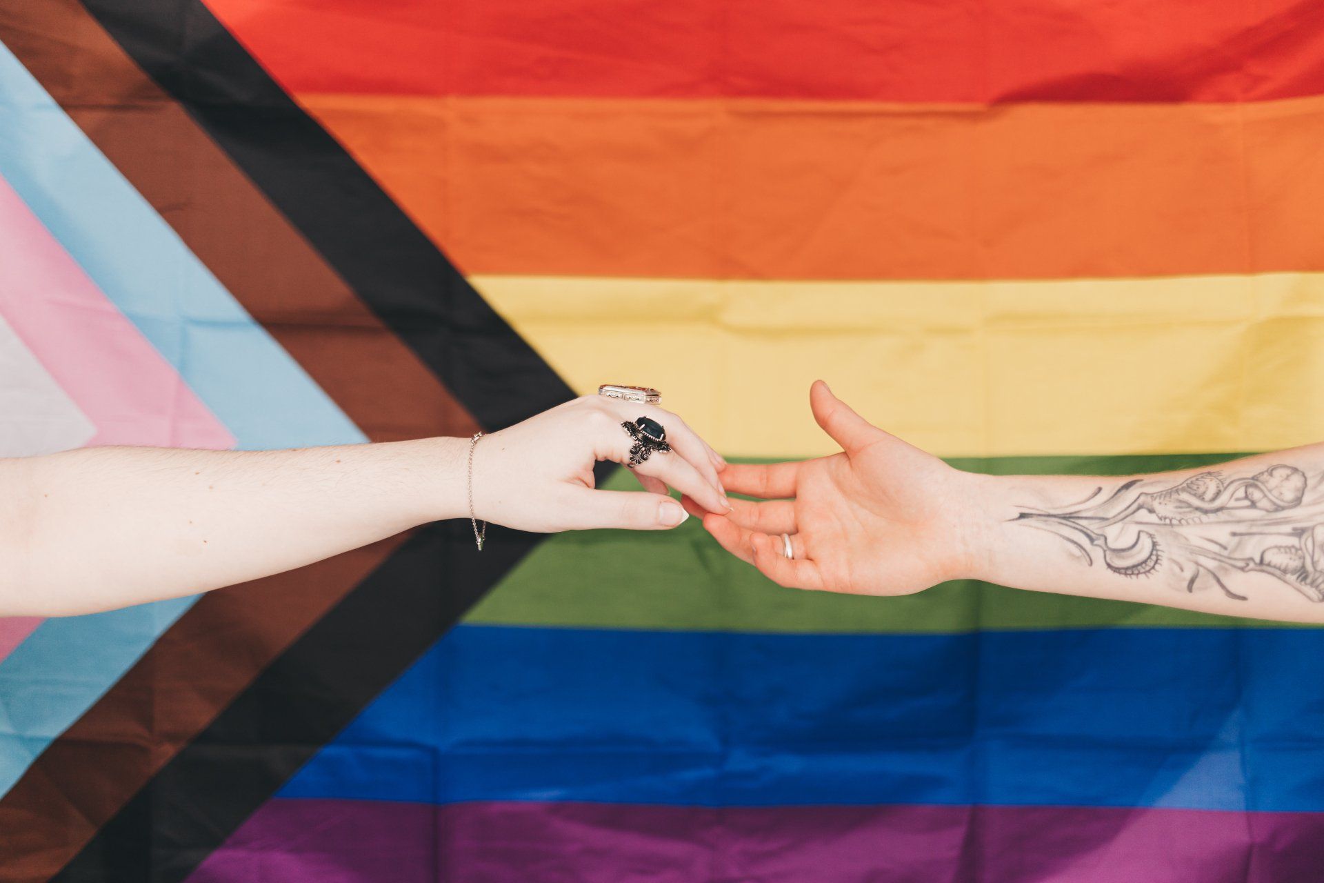Two hands reaching toward each other in front of a rainbow pride flag backdrop