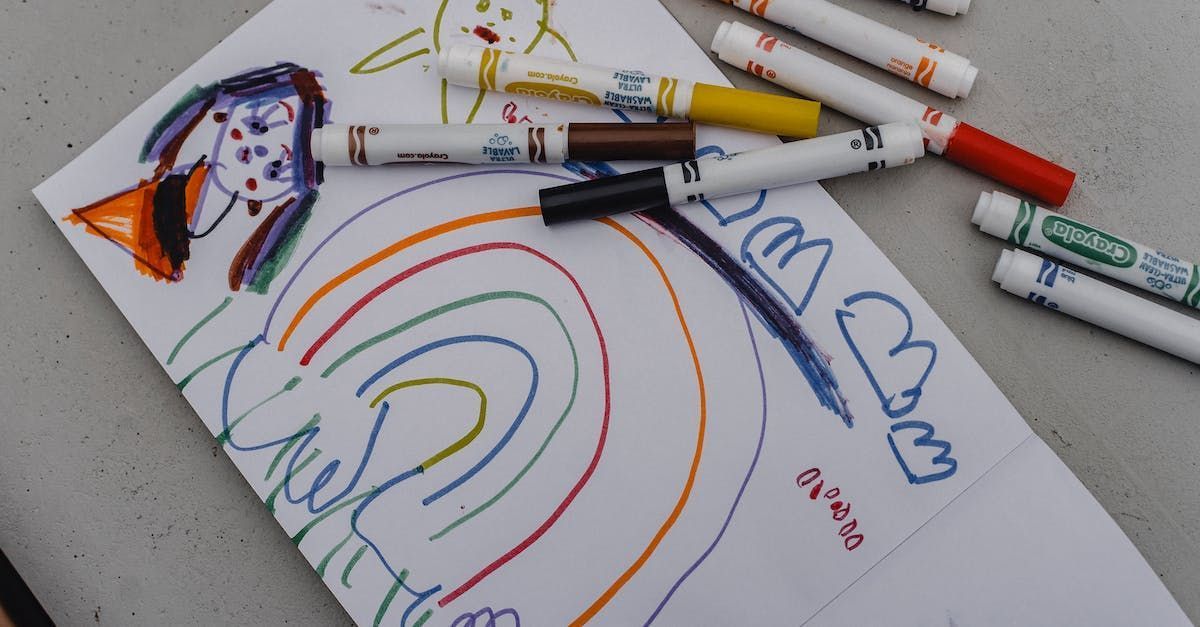 Children’s rainbow drawing on paper with markers scattered around it