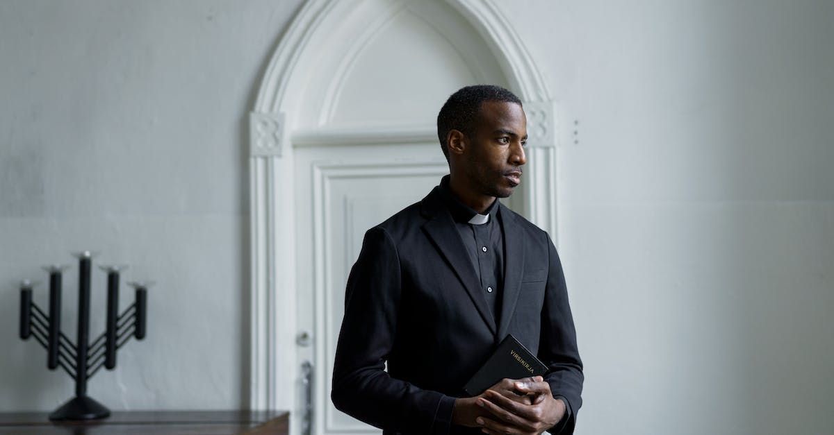 Man in a dark suit standing by an arched doorway in a bright room