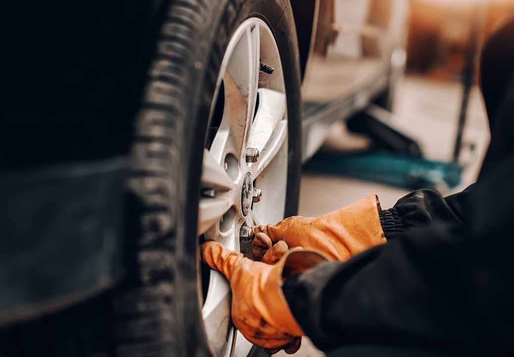 A man wearing orange gloves is changing a tire on a car.