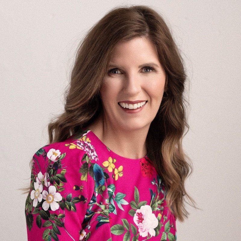 Woman with brown hair smiles, wearing a pink floral dress.