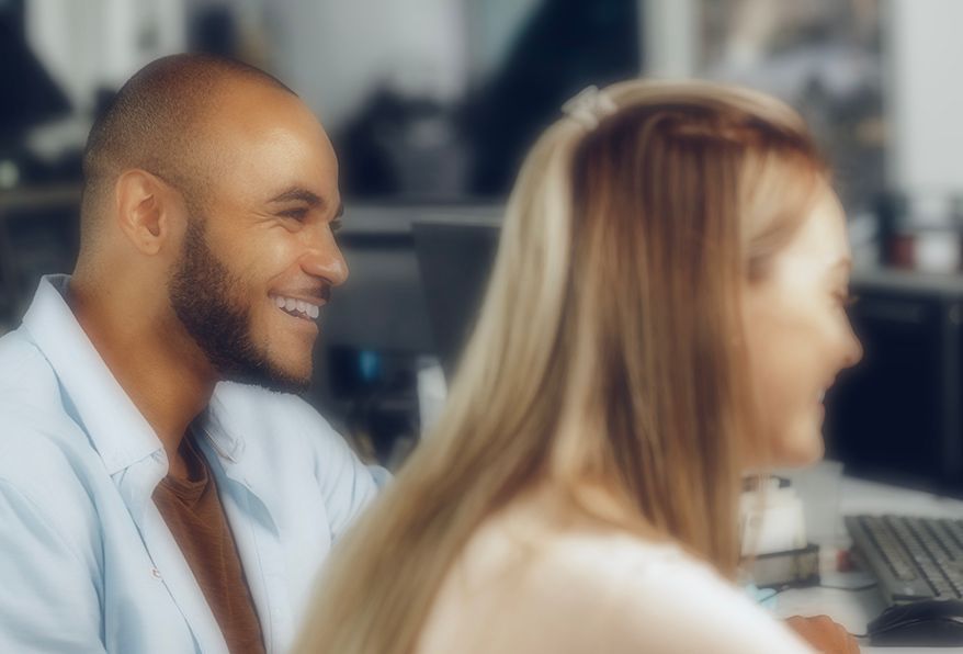Man smiling, looking towards a woman. Both appear to be in an office setting.