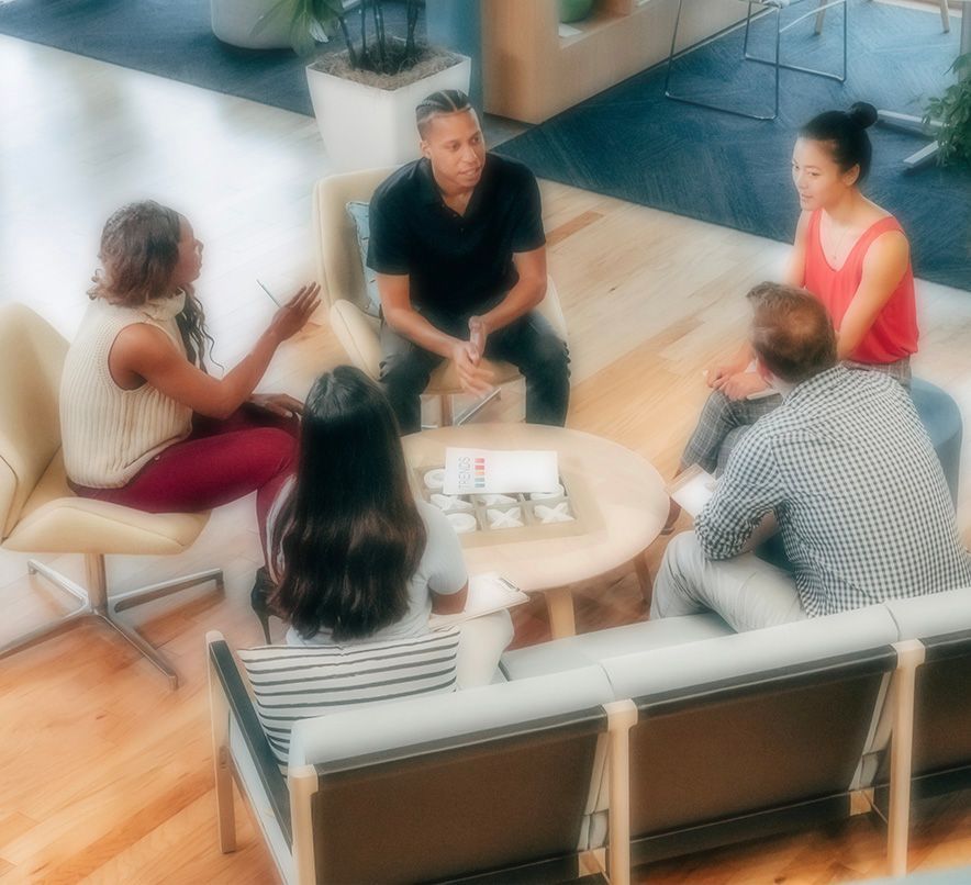 Group of people in casual wear seated around a table, engaged in a discussion in a modern office.