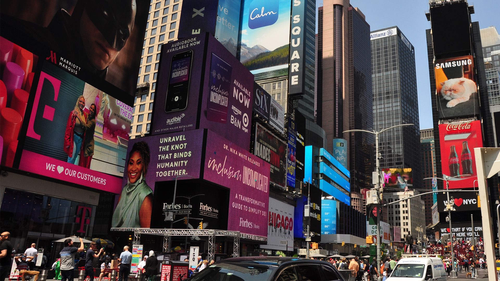 Times Square, NYC. Bright billboards on tall buildings with crowds, cars, and a clear blue sky.