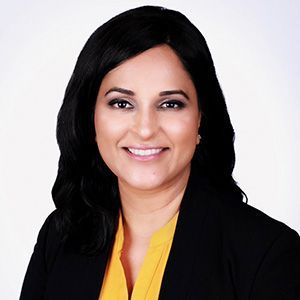 Woman in a black blazer and yellow shirt smiling at the camera.