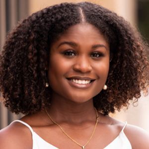 Woman with curly hair smiles, wearing a white top and gold necklace.