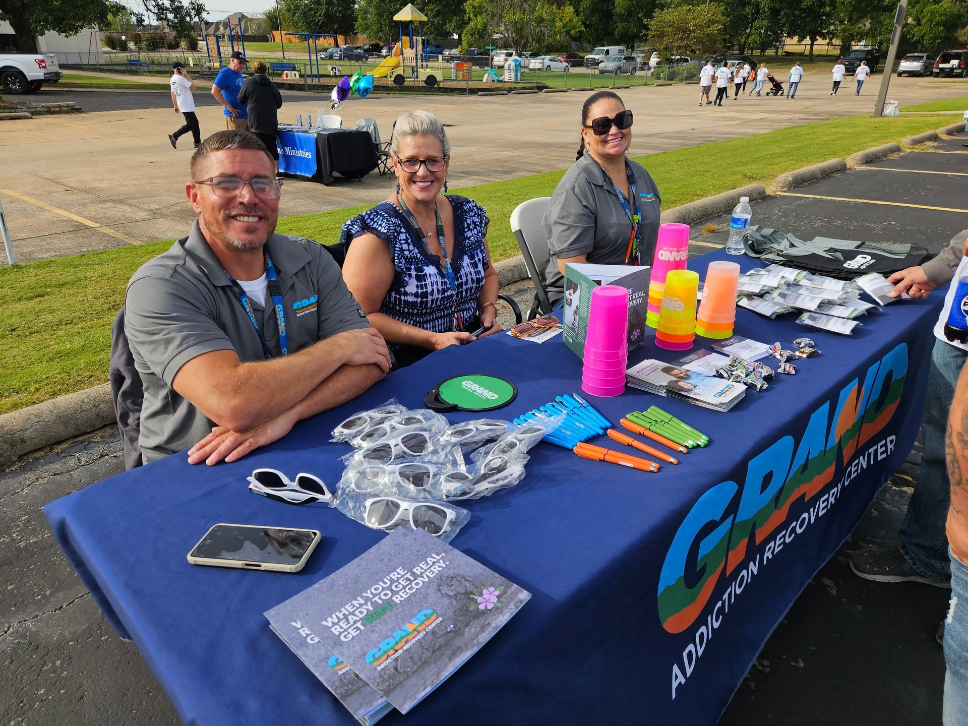 A group of people are sitting at a table in a parking lot.