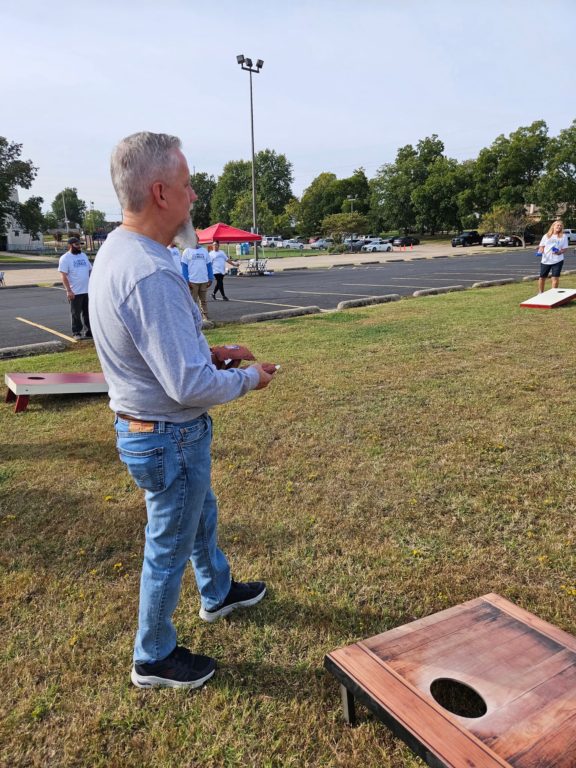 A man is standing in the grass playing cornhole in a park.