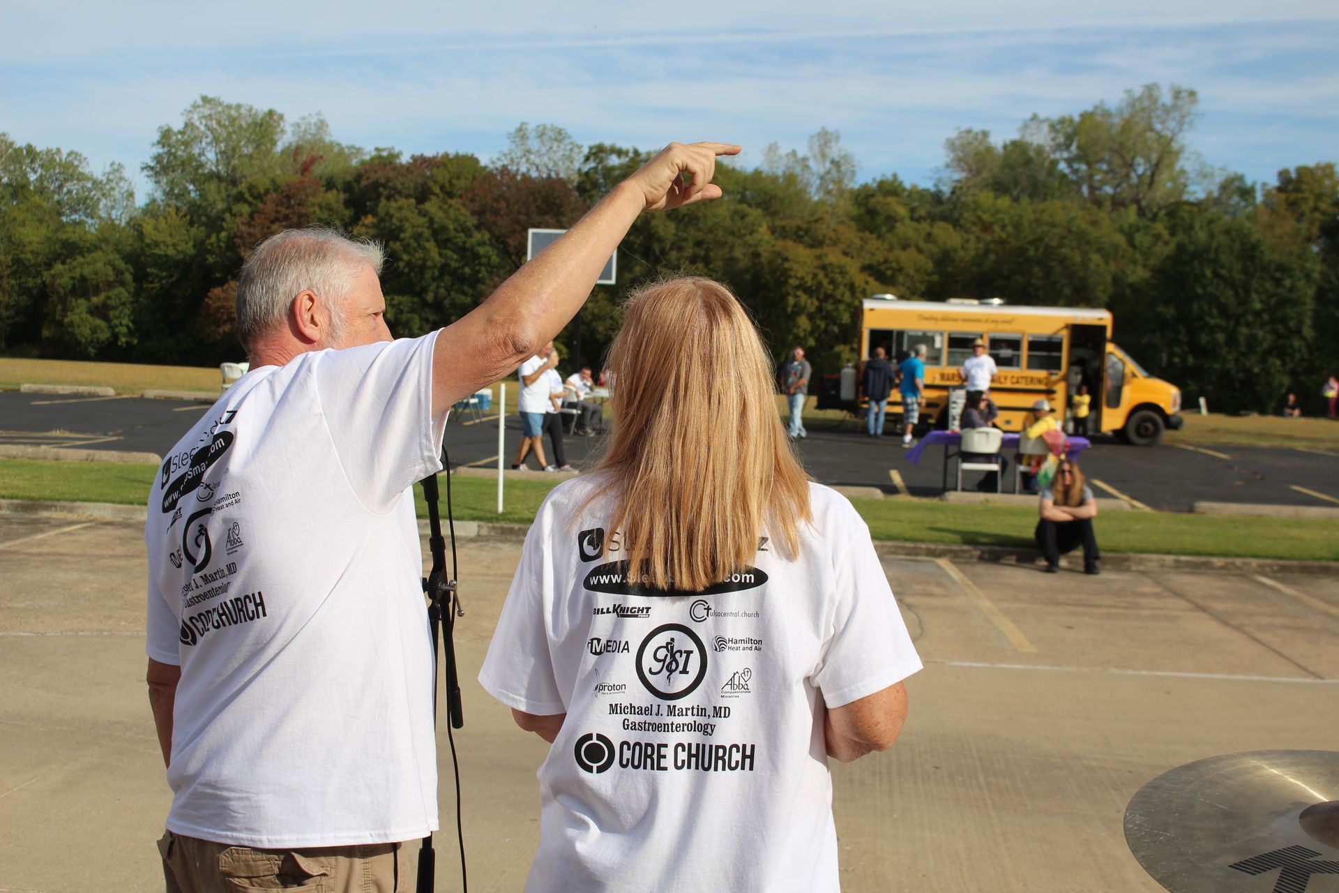 A man and a woman are standing in front of a yellow school bus.