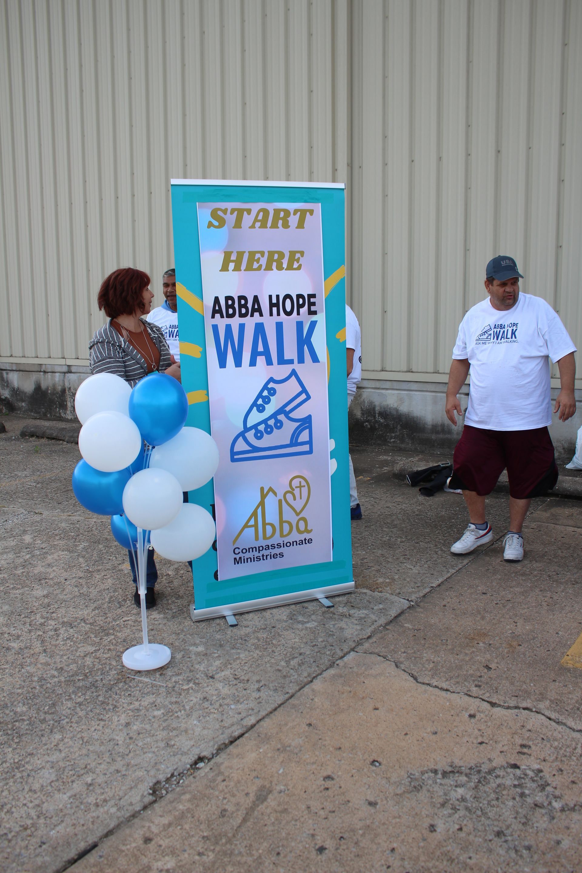 A group of people are standing in front of a sign that says `` start here abba hope walk ''.