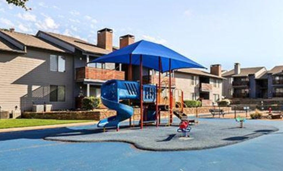 Apartment complex playground with blue shade canopy, slide, and climbing equipment on a rubber play surface