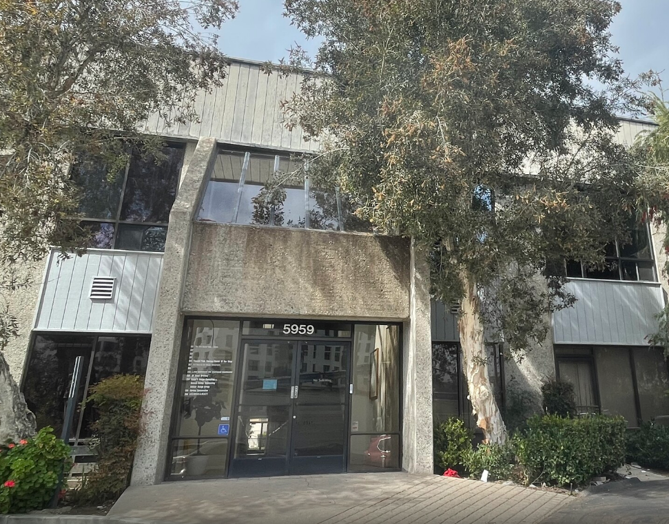 Modern office building entrance with trees and shrubs outside, seen in daylight.