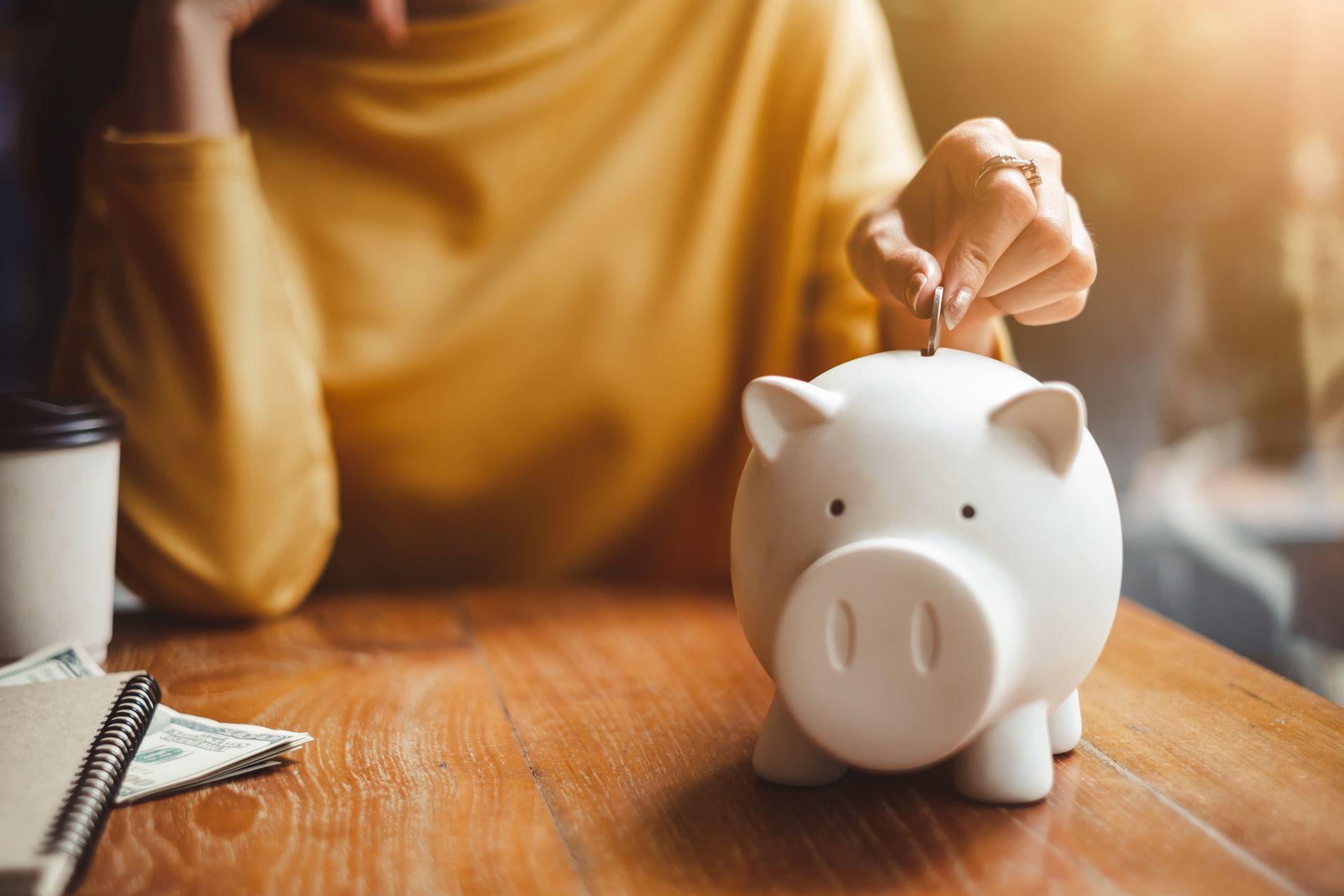 Person places a coin into a white piggy bank on a wooden table