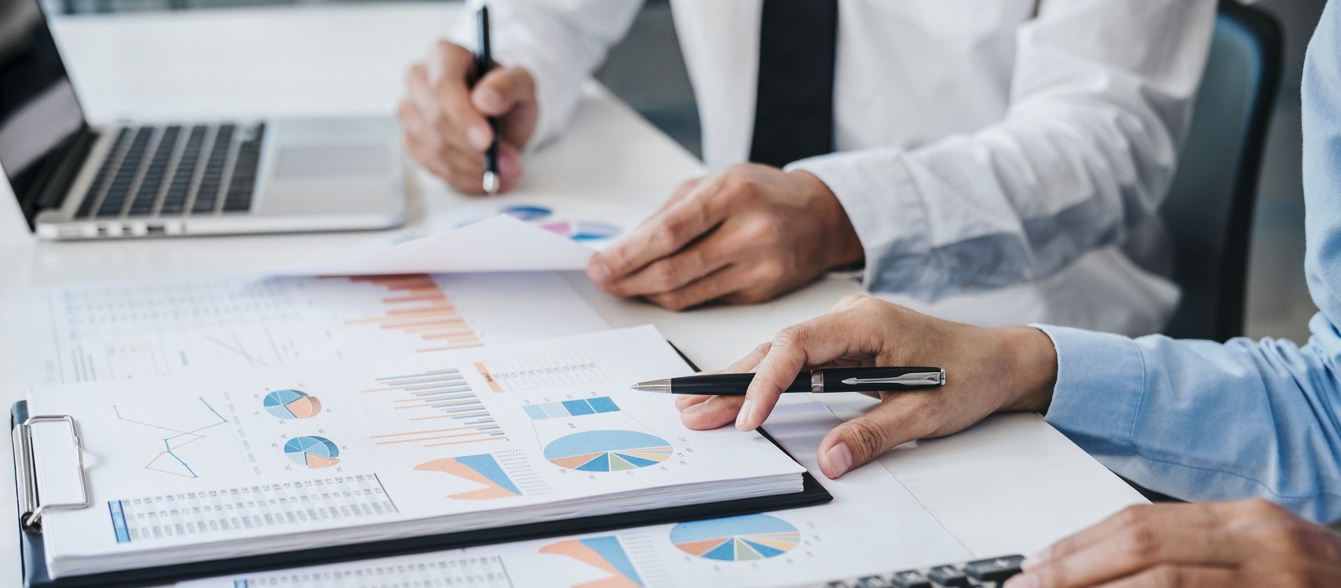Hands reviewing charts and graphs on a clipboard at a desk with a laptop nearby