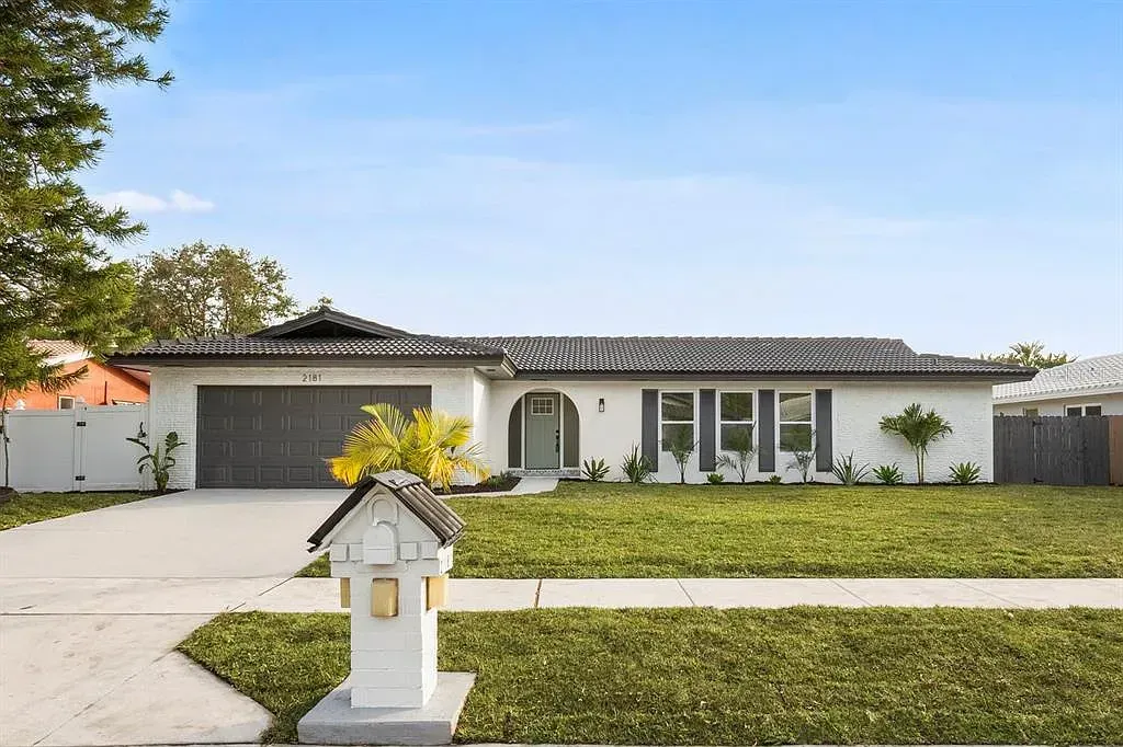 Single-story suburban house with a manicured lawn, driveway, and mailbox under a clear blue sky