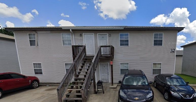 Apartment building exterior with central stairs and parked cars under a partly cloudy sky
