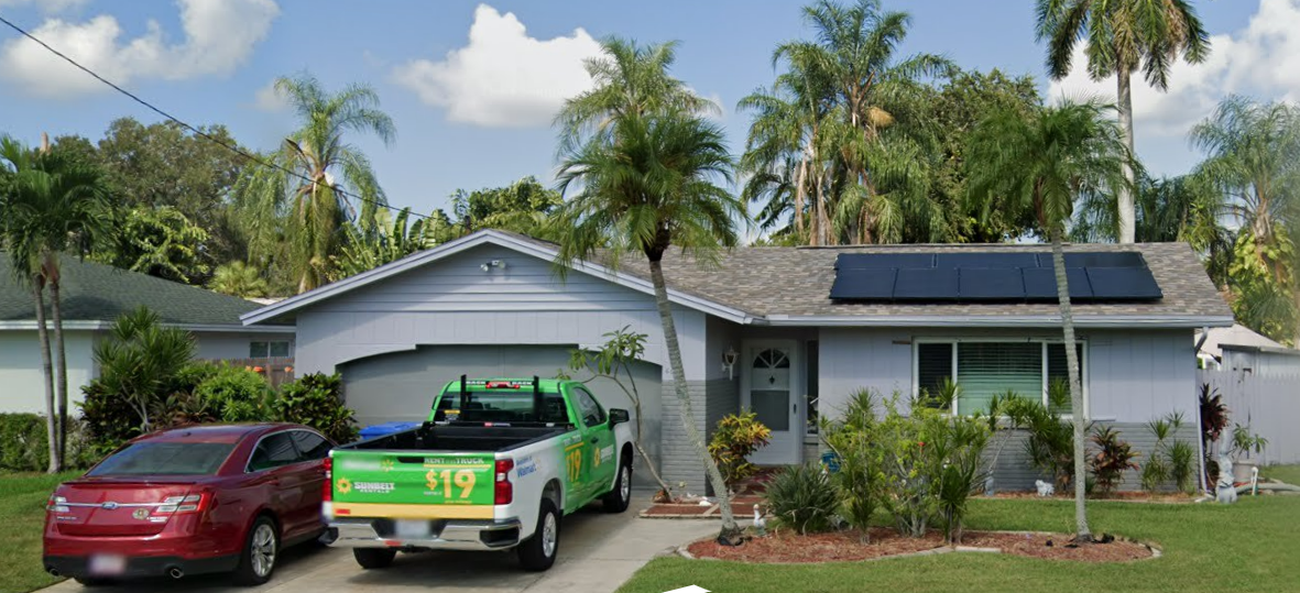 Single-story suburban home with solar panels, a red car, and a green pickup truck in the driveway.
