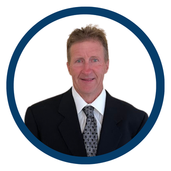 Man in a black suit and patterned tie against a white background, framed by a blue circle.