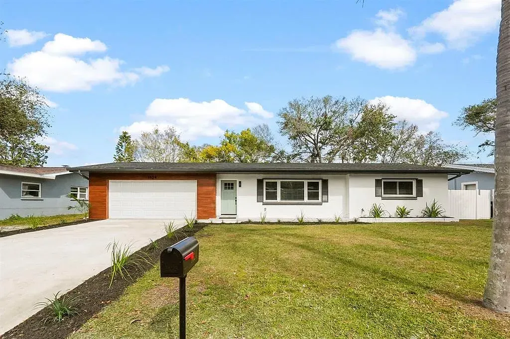 Single-story white house with a garage, front lawn, and mailbox under a partly cloudy sky