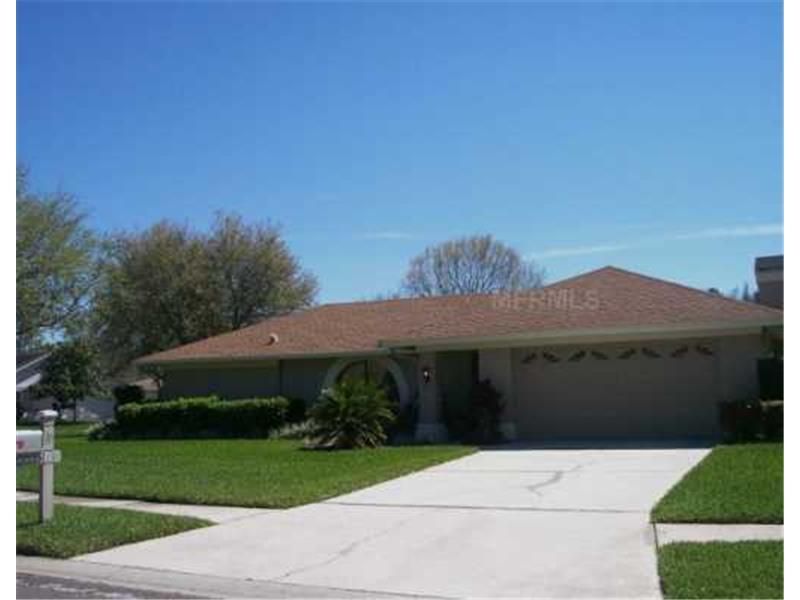 Single-story suburban house with a red roof, white driveway, and green lawn under a clear blue sky