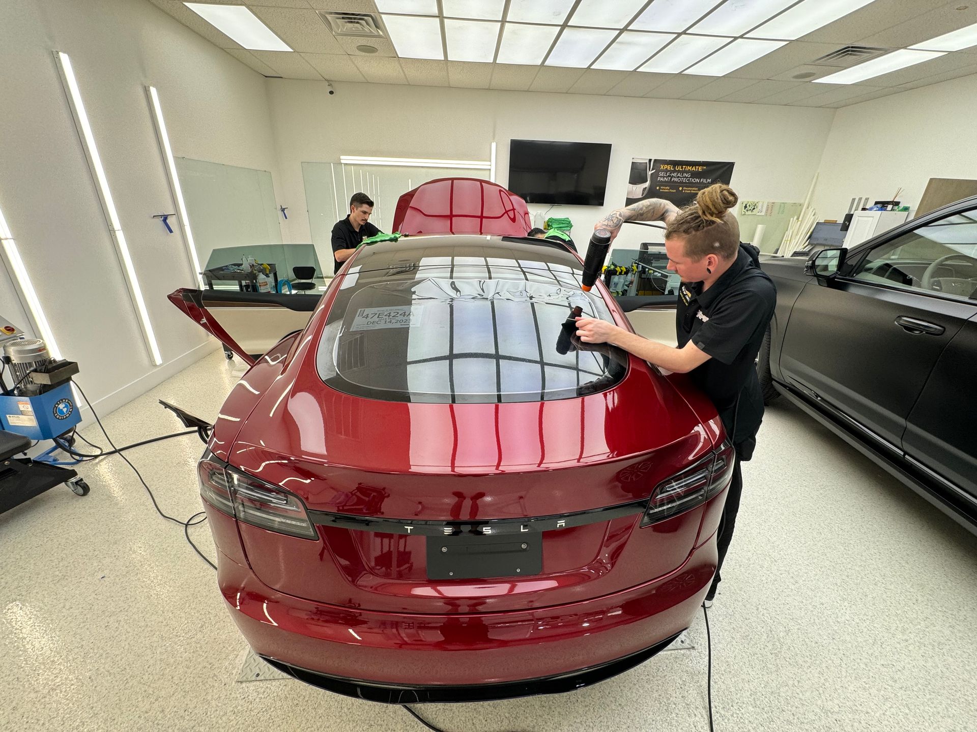 A man is working on a red tesla model s in a garage.