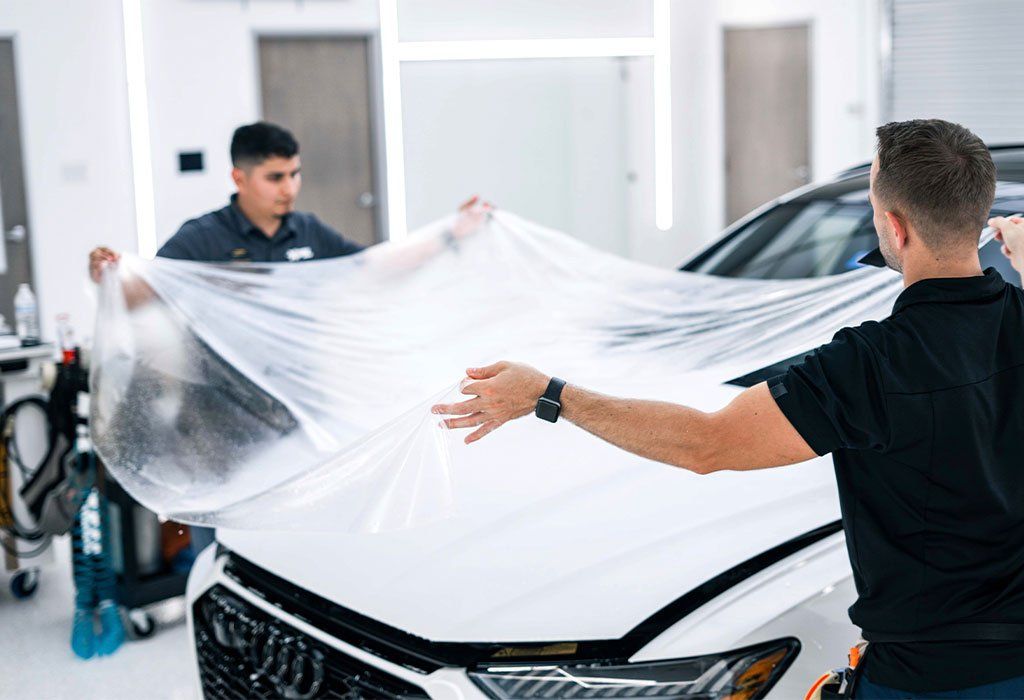 A man is wrapping a white car with plastic wrap.