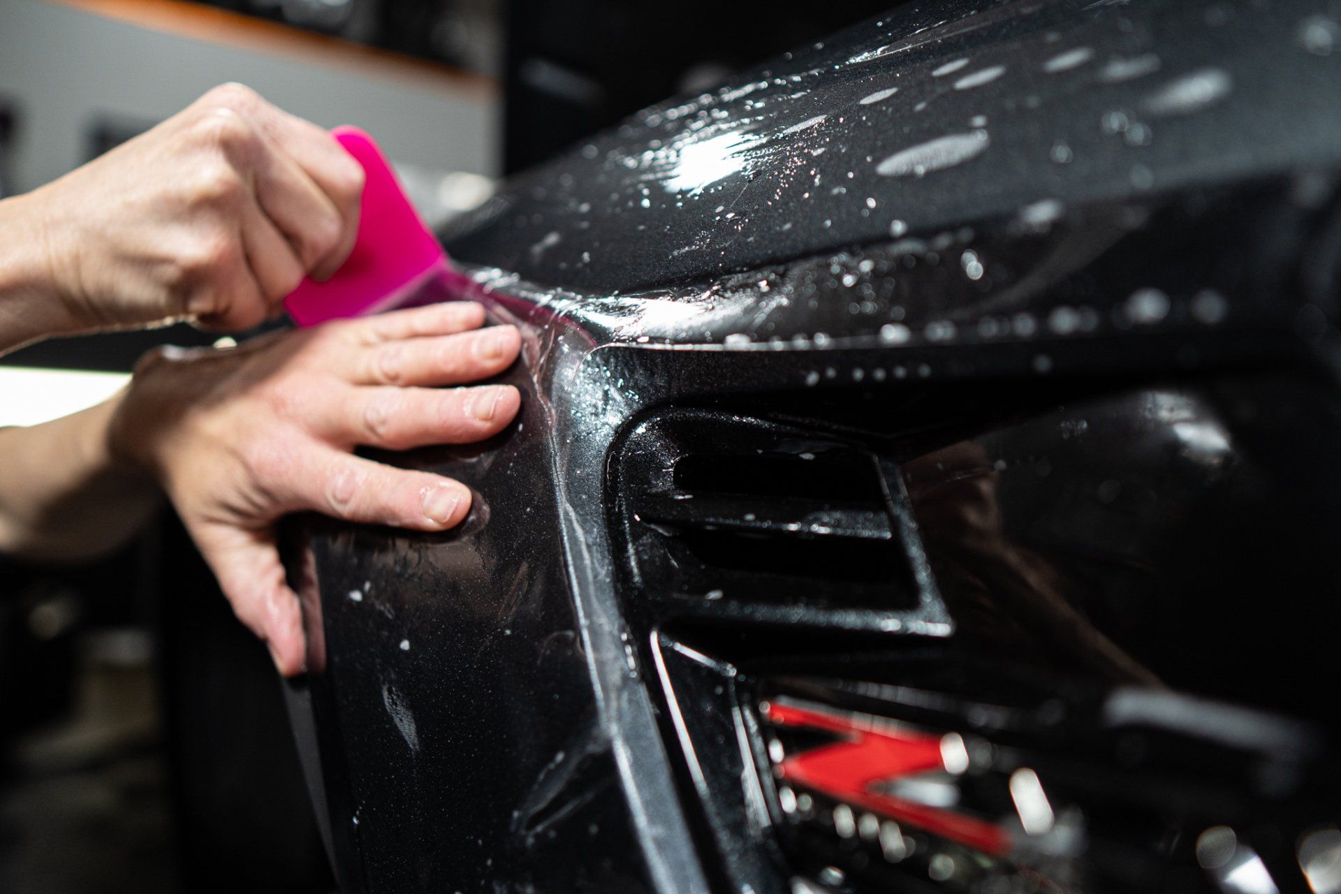 A person is applying a protective film to the front of a car.