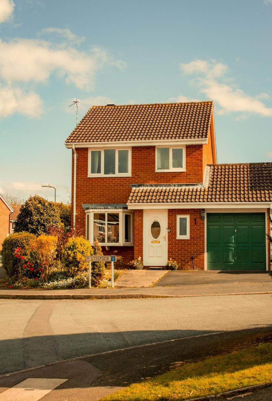 Two-story red brick house with green garage door on a quiet suburban street