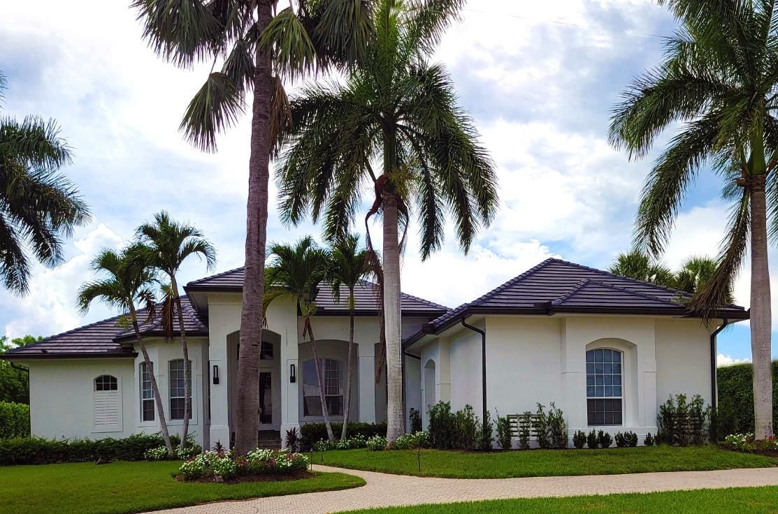 Single-story white house with a dark roof, palm trees, and a manicured lawn in a sunny tropical setting