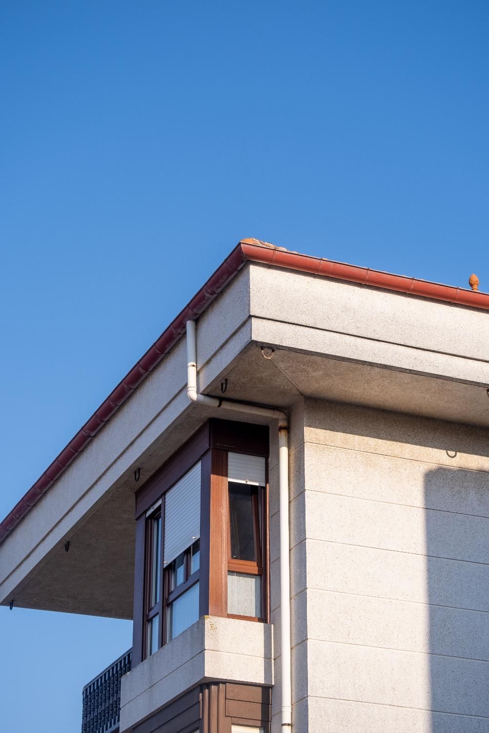 Modern building corner with white stucco walls, red roof trim, and large windows against a blue sky