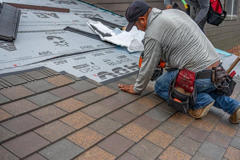 Worker installing roof shingles on a house roof.