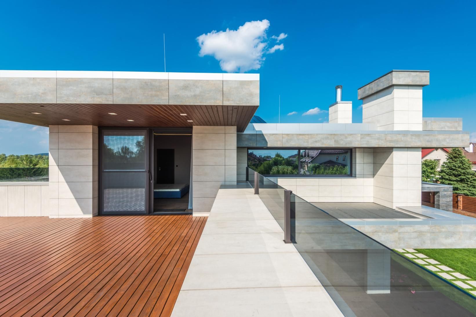 Modern rooftop terrace with wooden deck, glass railing, and minimalist concrete architecture under a blue sky