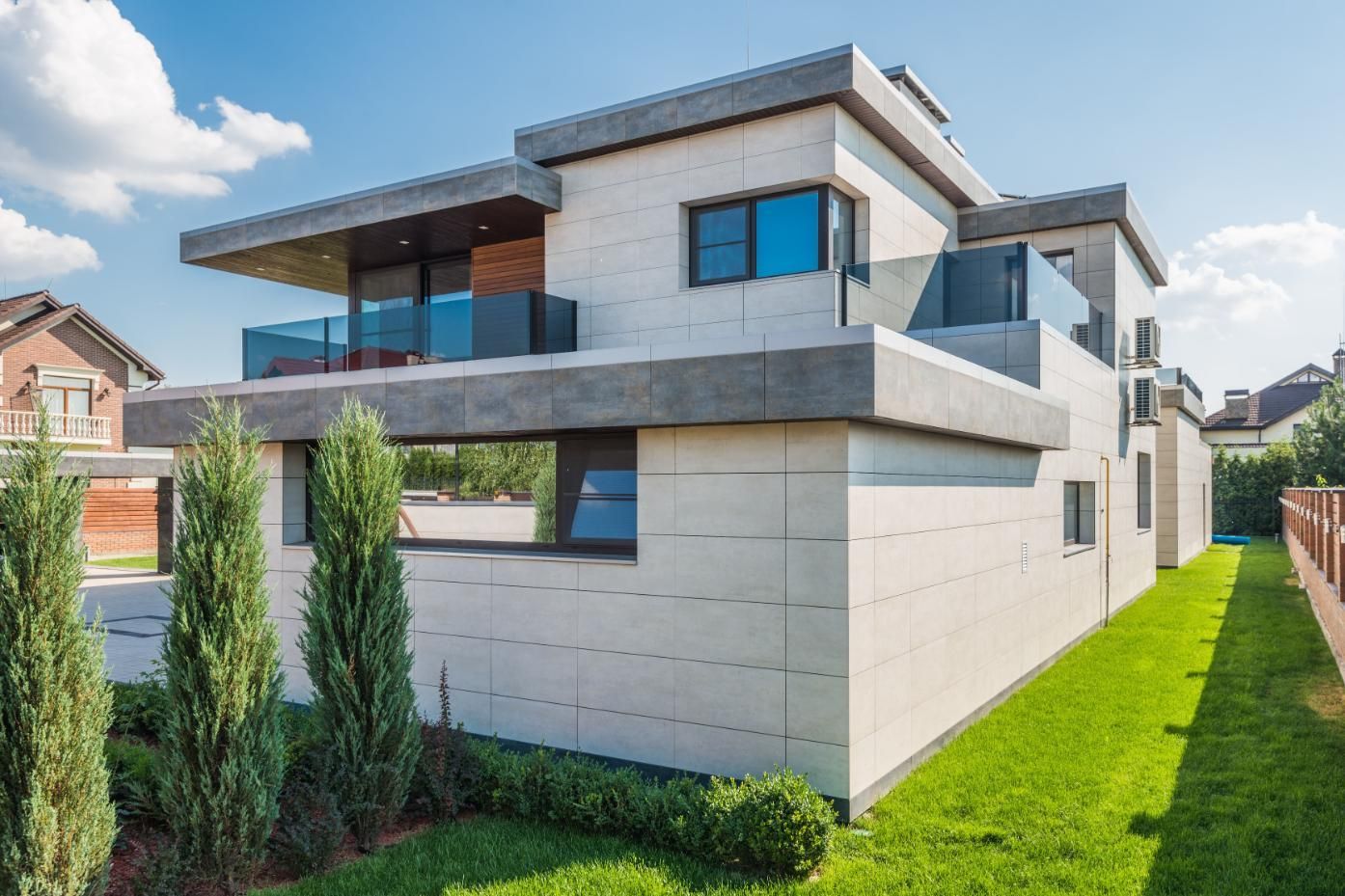 Modern two-story white house with large windows and a green lawn under a blue sky