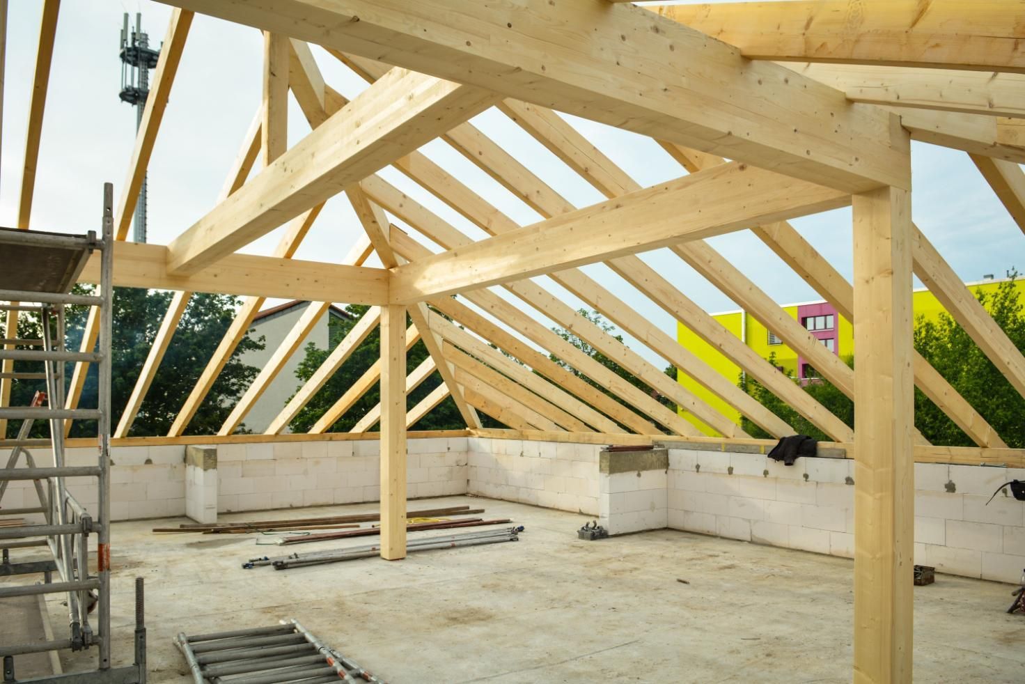 Partially built wooden roof trusses inside an unfinished house with concrete walls and a ladder