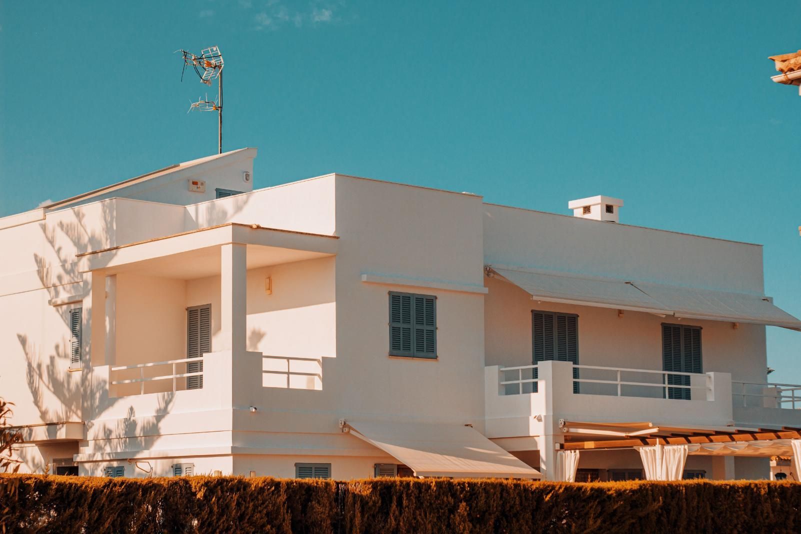 White modern house with balcony and teal sky, viewed from the street