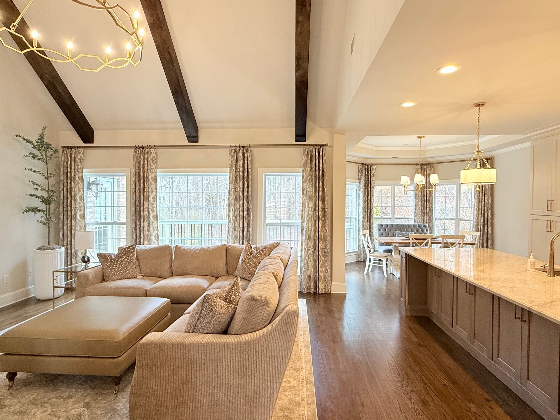 Bright open-concept living room and kitchen with beige furniture, wood beams, and island seating