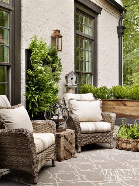 Wicker patio chairs with cream cushions beside a house and lush green plants