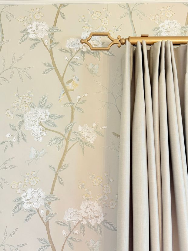 Floral wallpaper beside beige pleated curtains and a gold curtain rod bracket